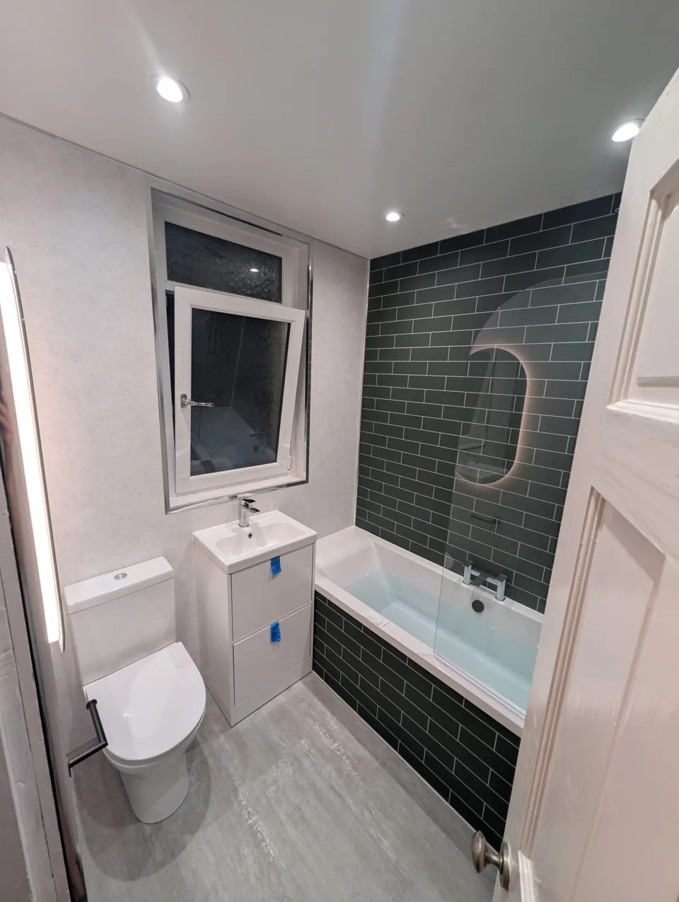 Fitted bath with green tiles and white bathroom furniture