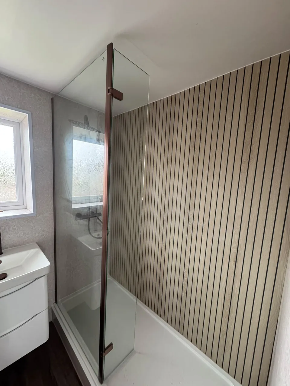 Glass shower enclosure beside a wood-effect feature wall